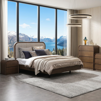 A modern bedroom set featuring a bed with a tufted headboard, matching wooden nightstands and dressers, a large gray area rug, and a framed botanical print, set against a backdrop of large windows showing a mountain and lake view.