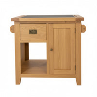 A small wooden kitchen bench cabinet or side table made of natural oak wood, featuring a single drawer with a brass pull, a lower open shelf, and a dark rectangular top surface.